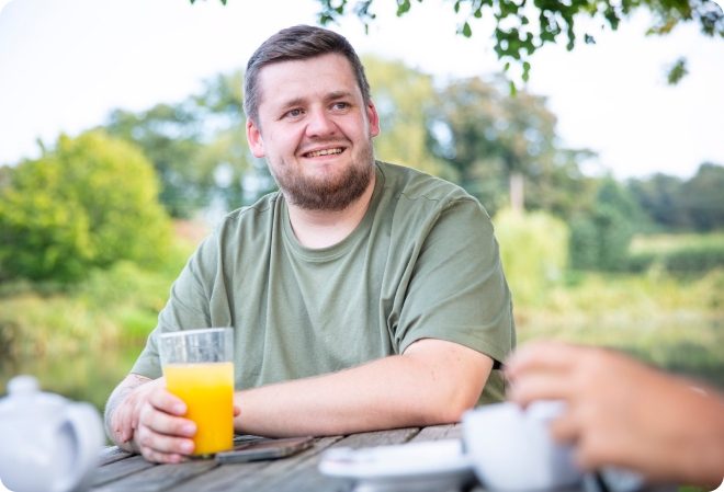 Adrian in a green t-shirt with an orange juice smiling