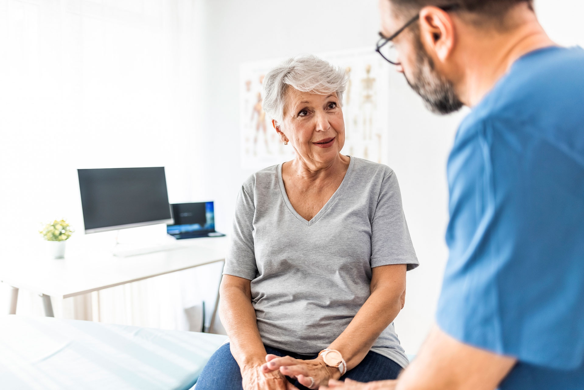 Ältere Patientin im Beratungsgespräch mit einem Arzt in einer hellen Arztpraxis.