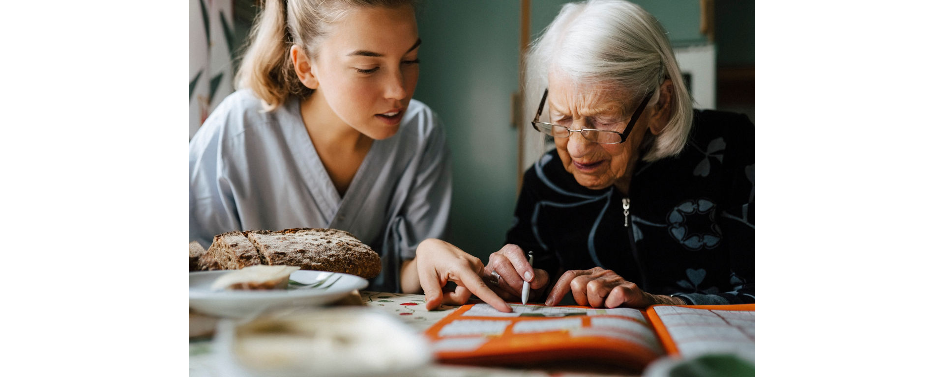 A young woman and an older woman sit together and play a crossword puzzle