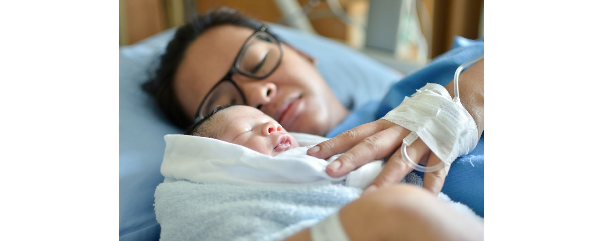 A women holds a newborn baby to her chest. She awaits a hospital blood glucose point of care test