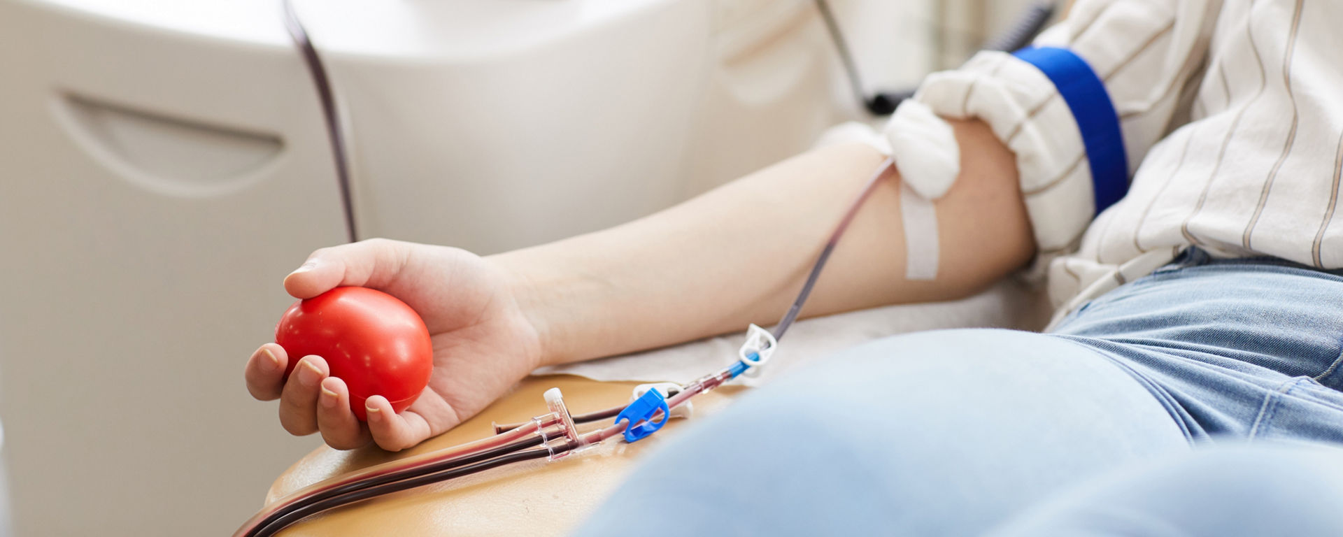 Close-up of female donor with ball in her hand and in catheter in her arm donating blood at hospital