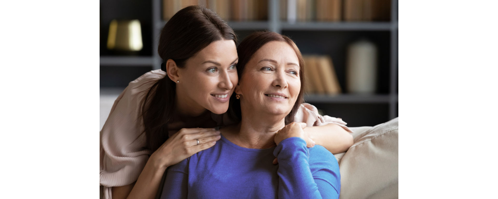 A daughter supporting her mother, who has an Alzheimer's diagnosis, in a living room. 