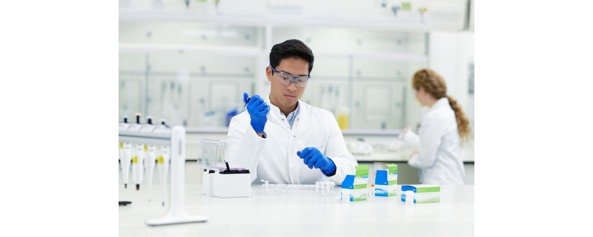 A lab technician wearing a lab coat sitting at a laboratory bench pipetting NGS sample prep reagents