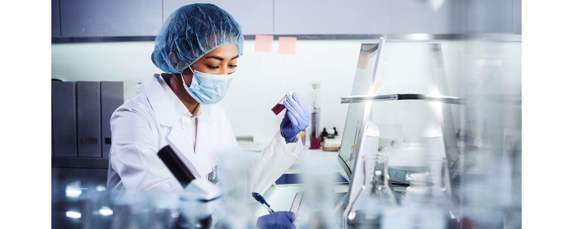 A female lab technician sitting and writing about a test specimen in her hand