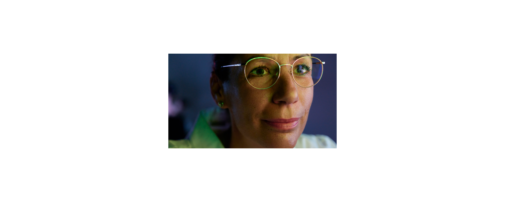 A scientist wearing glasses, focusing on a DNA image on an unseen computer screen