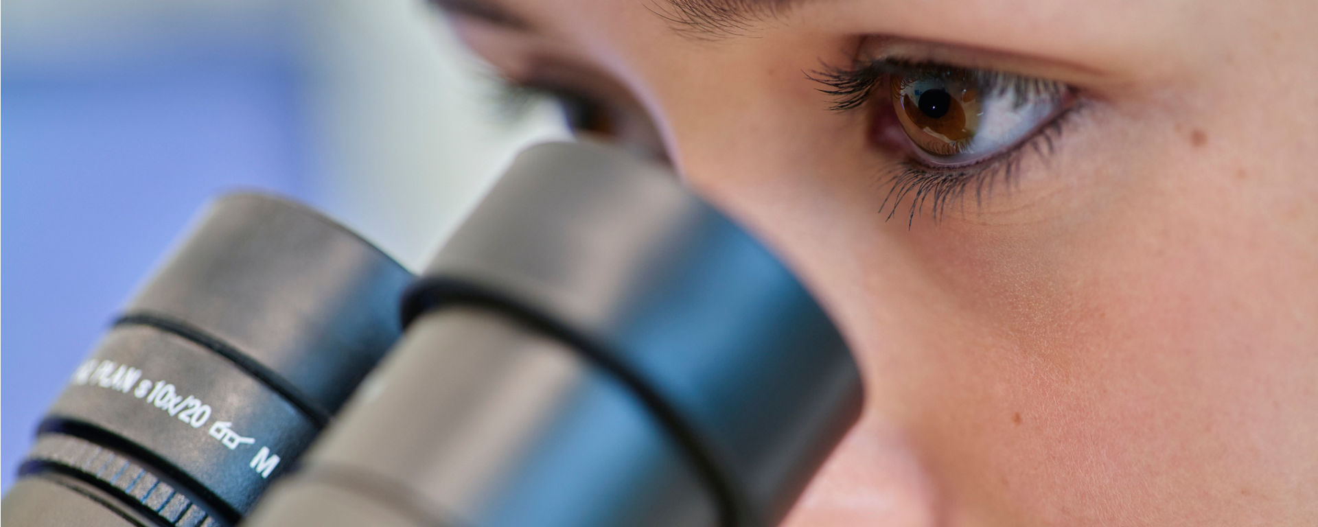 Researcher from CustomBiotech has a deep focused expression and is peering into a microscope within a laboratory setting