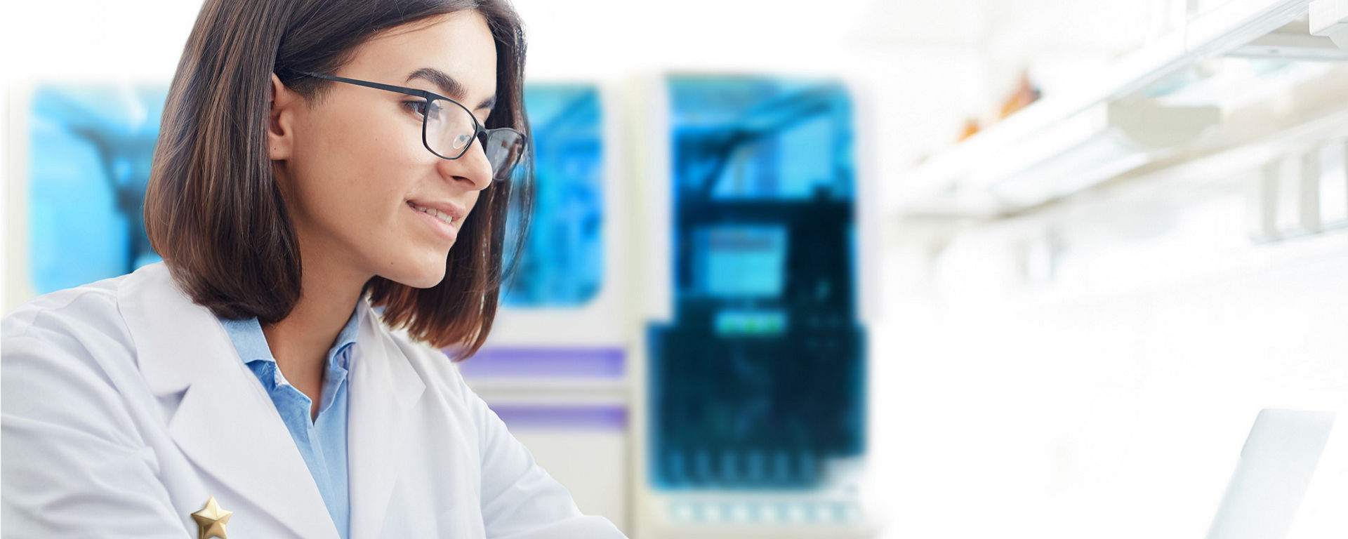An HCP in a lab coat sits at her bench on a laptop- A cobas coagulation assay sits on her bench in the forefront  