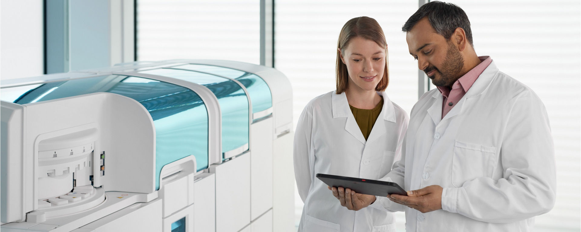 Two lab technicians discuss mass spectrometry results in front of a cobas i 601 analyzer