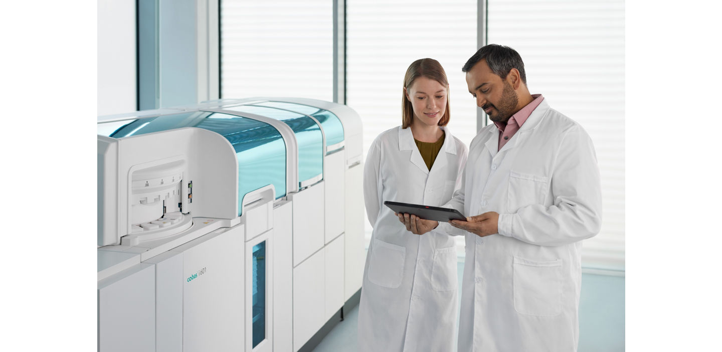 Two lab technicians discuss mass spectrometry results in front of a cobas i 601 analyzer