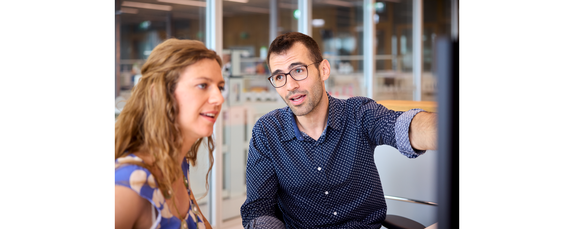 Two scientists discussing an NGS panel design displayed on a computer screen against a laboratory background