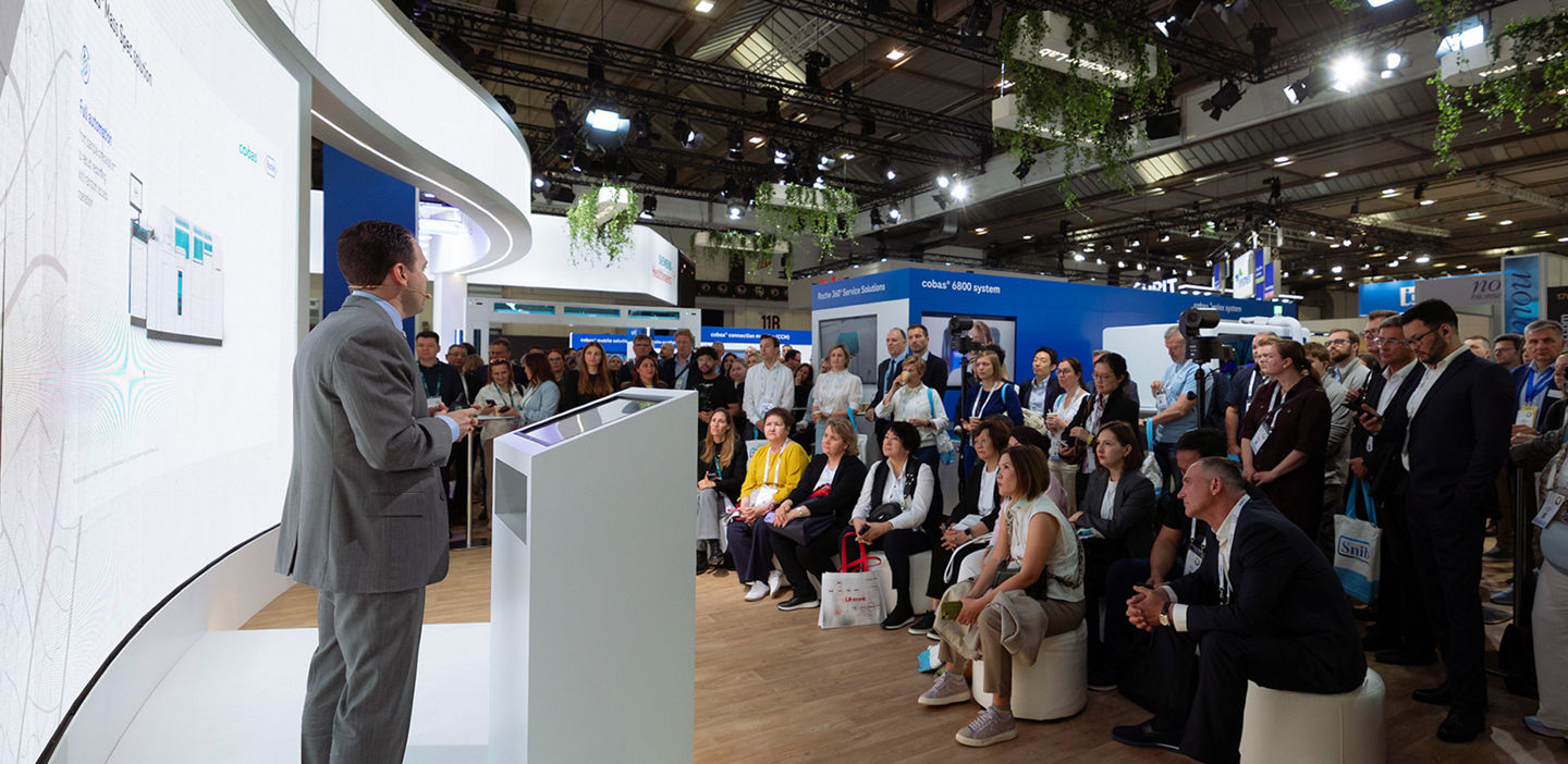 A speaker presenting at the Roche Booth at the EuroMedLab congress 2025. An audience is following the prensentation