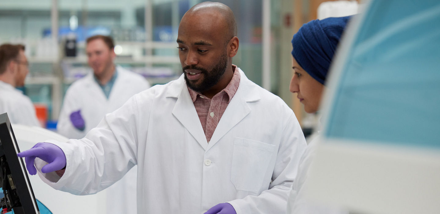 Two lab professionals looking at the screen of a lab device and having a discussion.