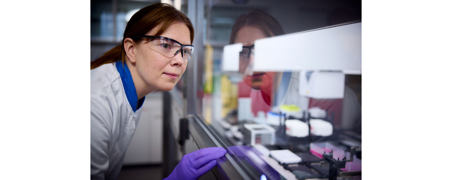 A laboratory technician wearing safety glasses inspects the reagents and consumables in an automated liquid handling system