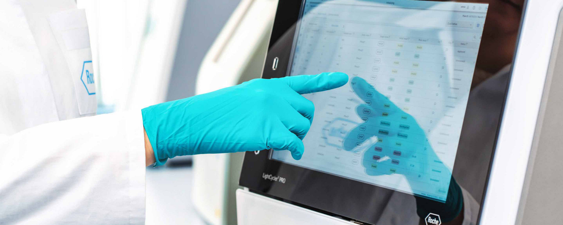Lab technician is touching the screen showing TIB MiolBiol assays on a Roche instrument with gloves on